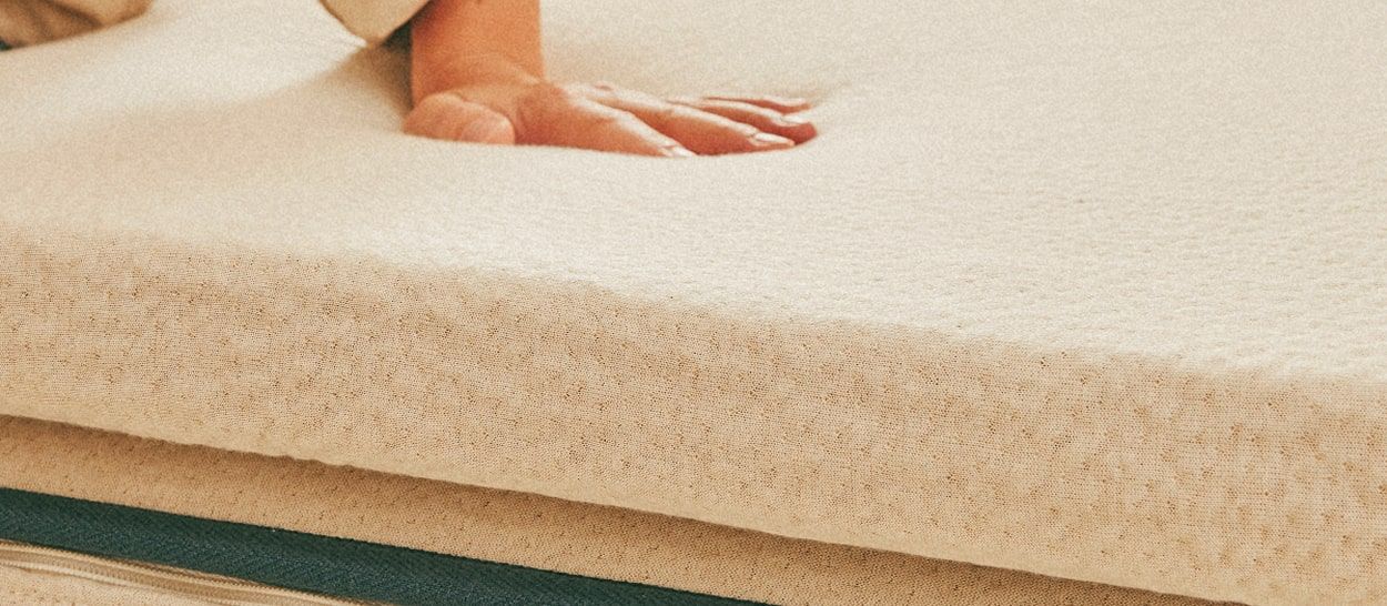 Main posée sur un surmatelas naturel Kipli illustrant le confort moelleux et la douceur du Tencel