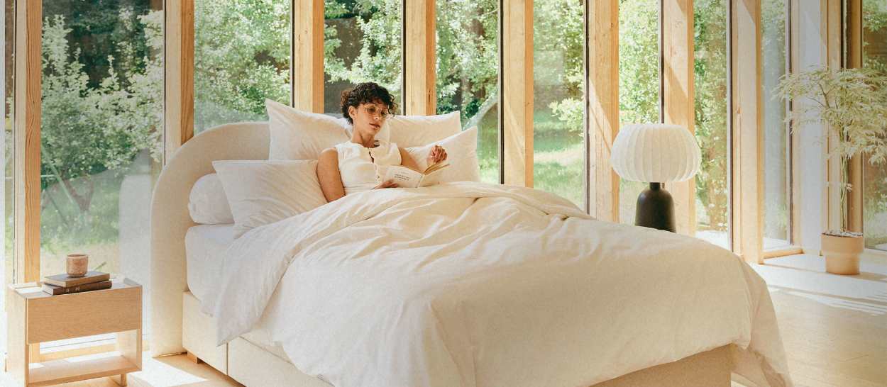 Personne lisant dans un lit, soutenue par plusieurs coussins, illustrant le confort par strates dans un coin lecture.