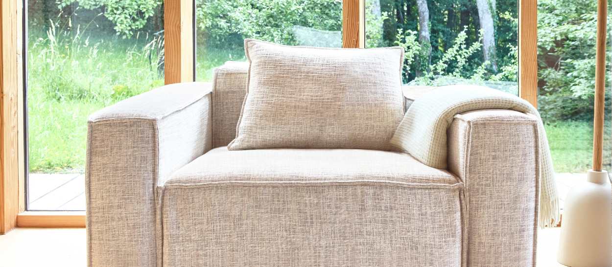 Fauteuil clair placé devant une grande baie vitrée, baigné de lumière naturelle, pour créer un coin lecture calme et lumineux.