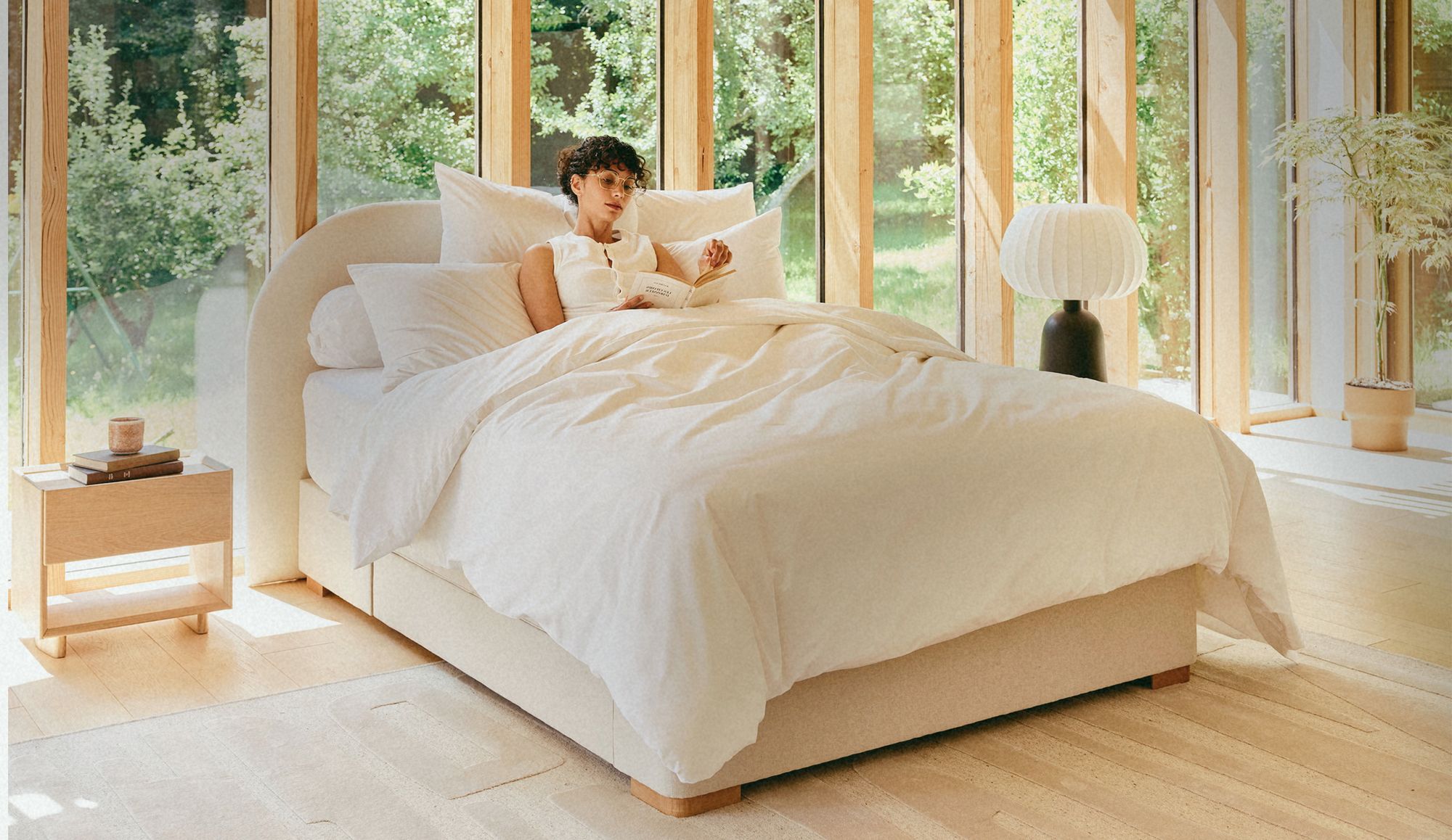 Femme lisant calmement dans un lit aux draps en fibres naturelles, lumière douce du soir dans une chambre rangée qui invite au rituel du coucher.