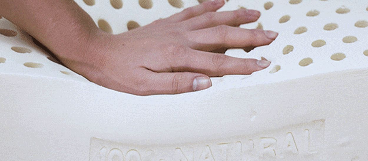 Main exerçant une pression sur un bloc de latex naturel perforé, illustrant la souplesse, la résilience et la respirabilité du matériau.