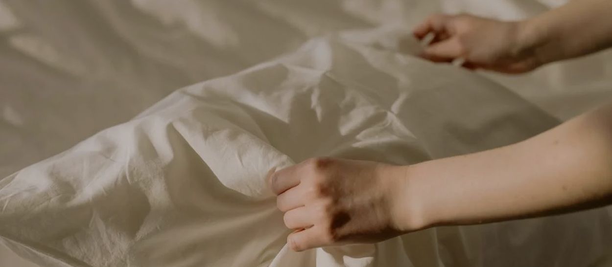 Mains arrangeant un drap beige sur un lit, en gros plan