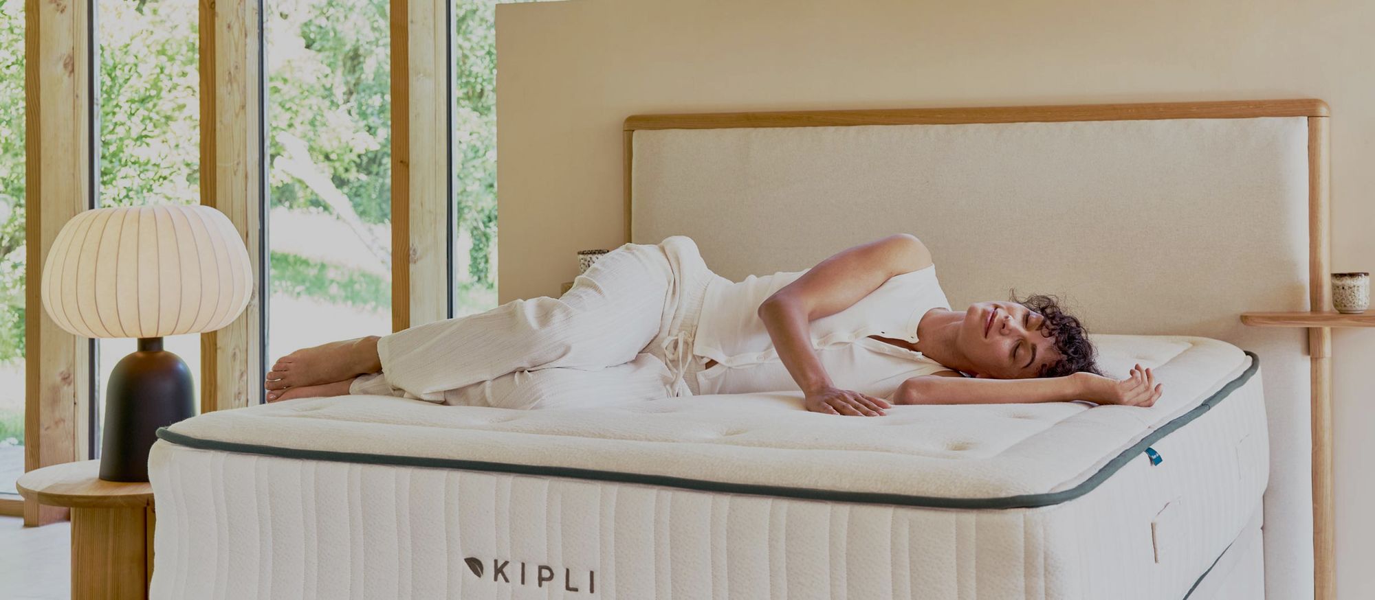 Personne allongée sereinement sur un matelas Kipli en latex naturel, chambre lumineuse en bois, ambiance douce du matin.