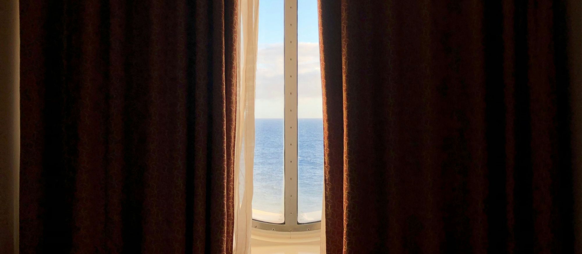Rideaux entrouverts laissant entrer la lumière du matin par une fenêtre donnant sur la mer, ambiance douce propice à l’éveil naturel.