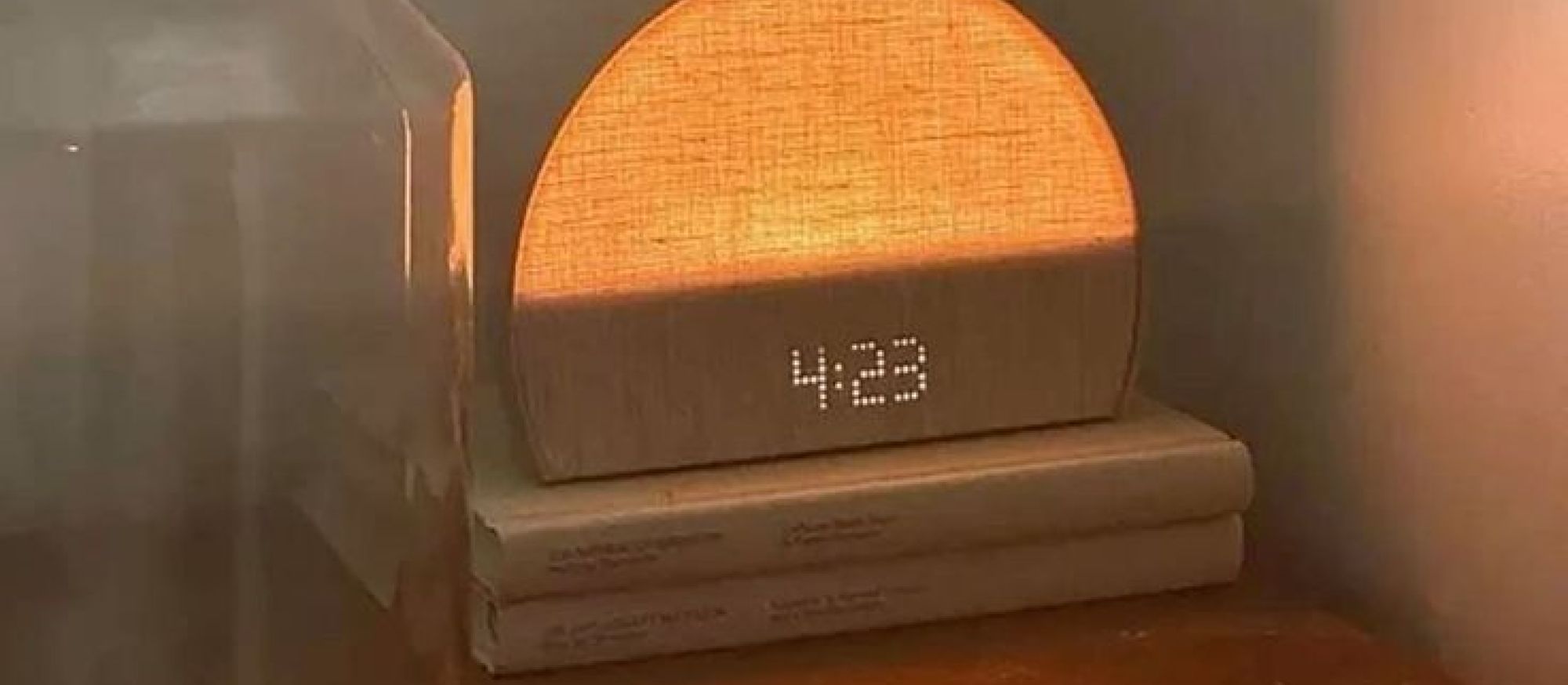 Simulateur d’aube posé sur des livres, affichage 4:23, lumière ambrée douce sur table de chevet pour un réveil progressif.