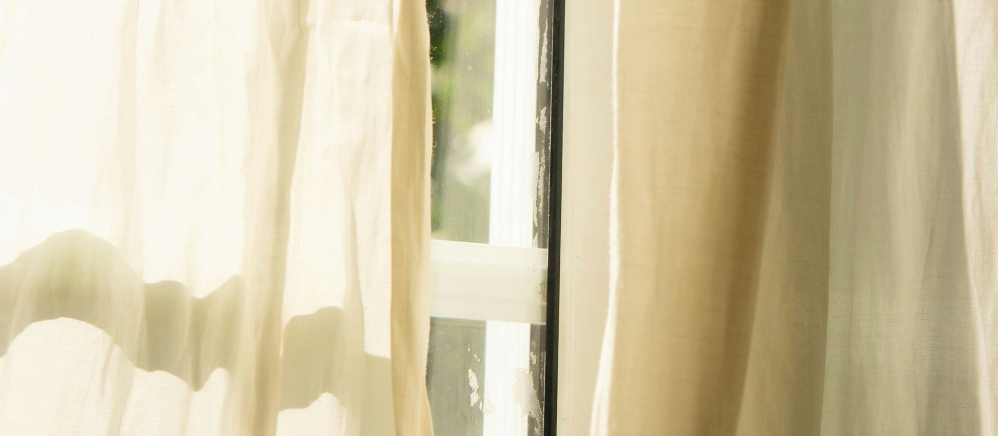 Voilages clairs filtrant la lumière du matin à travers une fenêtre entrouverte, ambiance douce qui favorise l’éveil naturel.