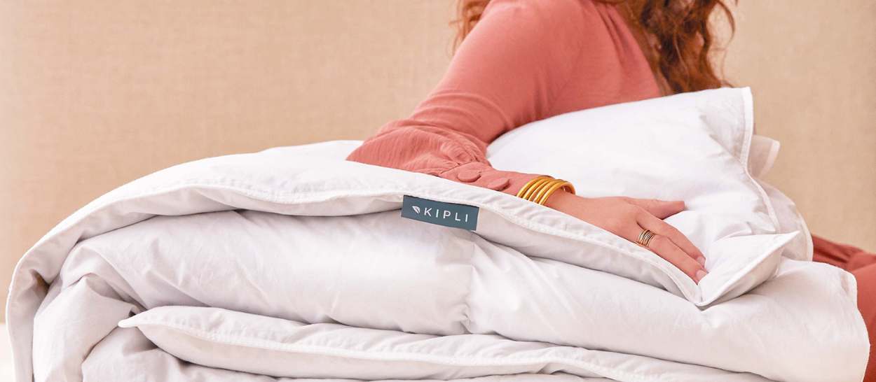 Femme appuyée sur une couette en duvet et plumettes recyclés Kipli pliée, idéale pour l’hiver