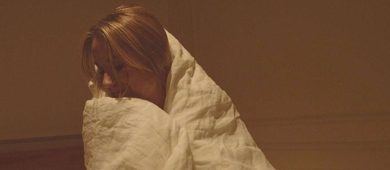 Femme blottie dans une couette chaude dans une chambre tamisée, prête à affronter l’hiver