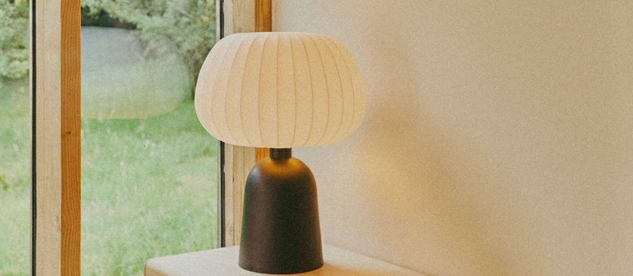 Lampe à poser Hikari au large abat-jour écru près d’une fenêtre, diffusant une lumière douce dans la chambre