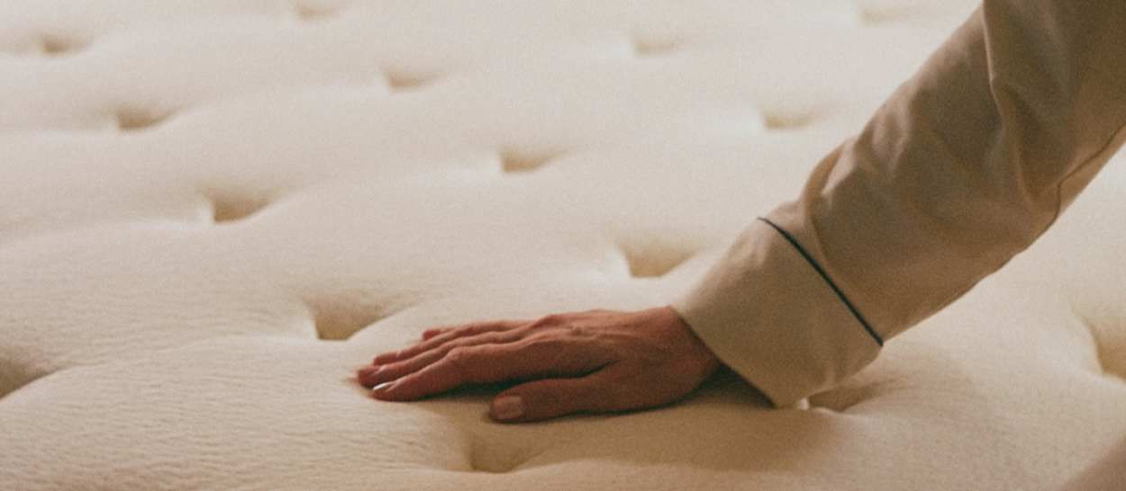 main posée sur la surface moelleuse d’un matelas Kipli en laine, montrant son confort et son accueil douillet