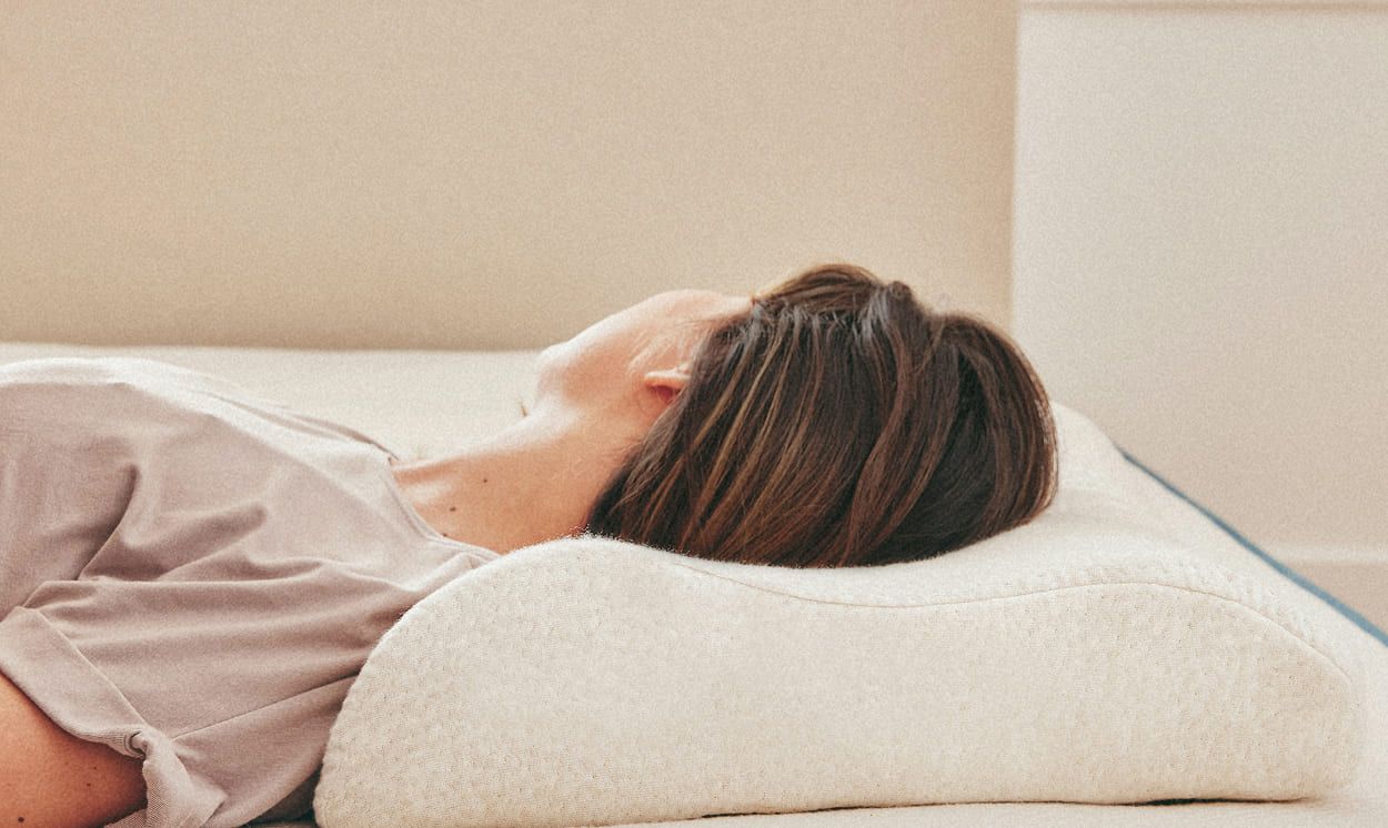 femme allongée sur le dos, tête posée sur un oreiller ergonomique en latex naturel soutenant la nuque en cas de hernie discale cervicale