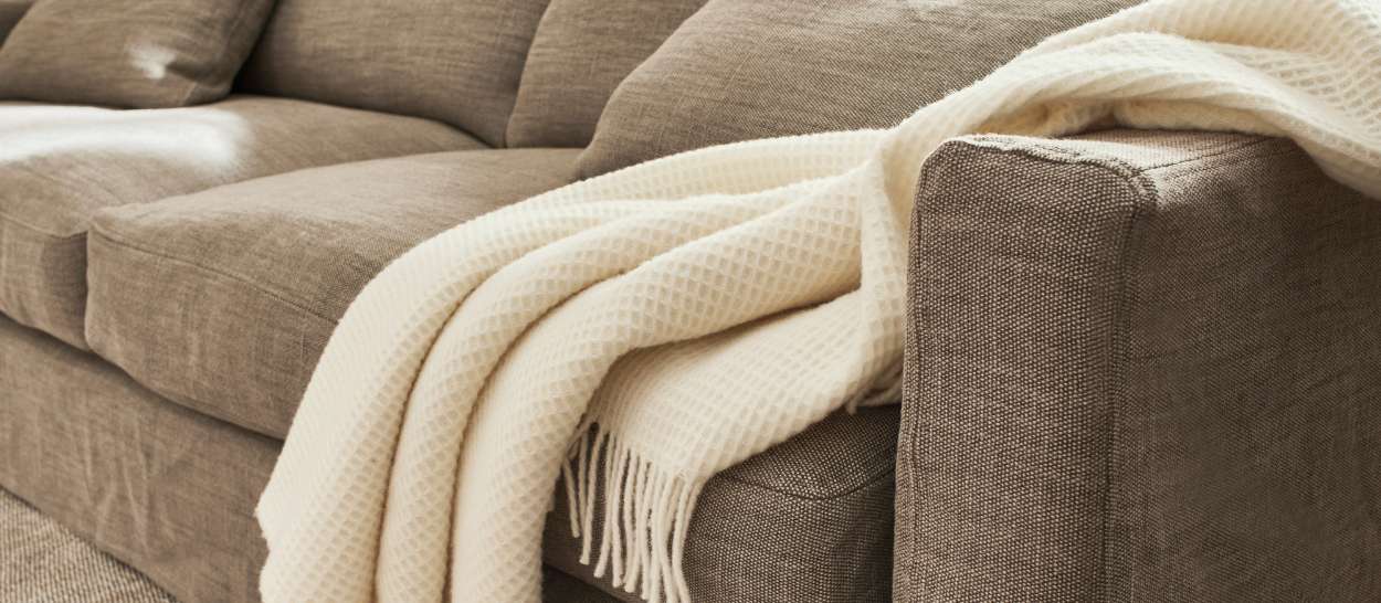 Plaid en gaze de coton biologique TIO écru posé sur un canapé en tissu, apportant une touche naturelle et élégante