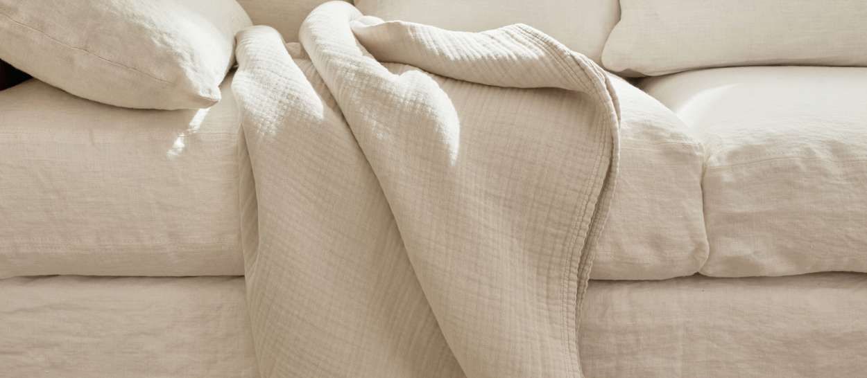 Plaid en laine d’alpaga écru ILLY posé sur un canapé, prêt à envelopper pour l’hiver