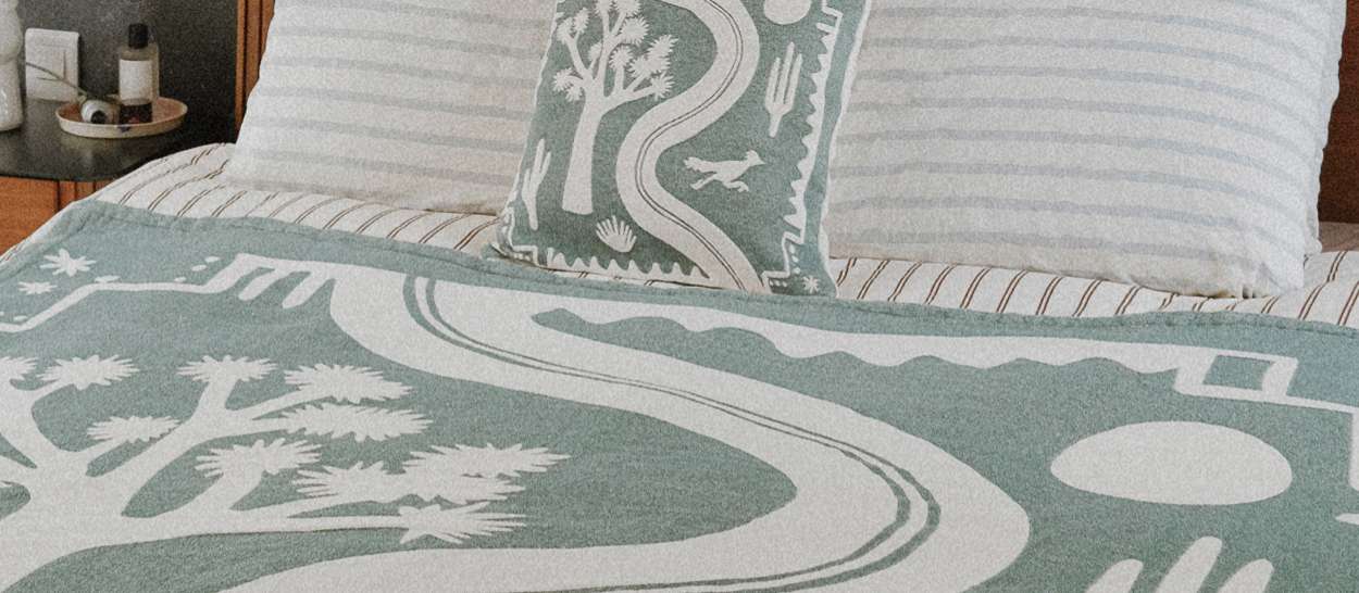 Plaid en coton jacquard Kipli x Coline vert et écru posé sur un lit, avec coussin assorti aux motifs graphiques