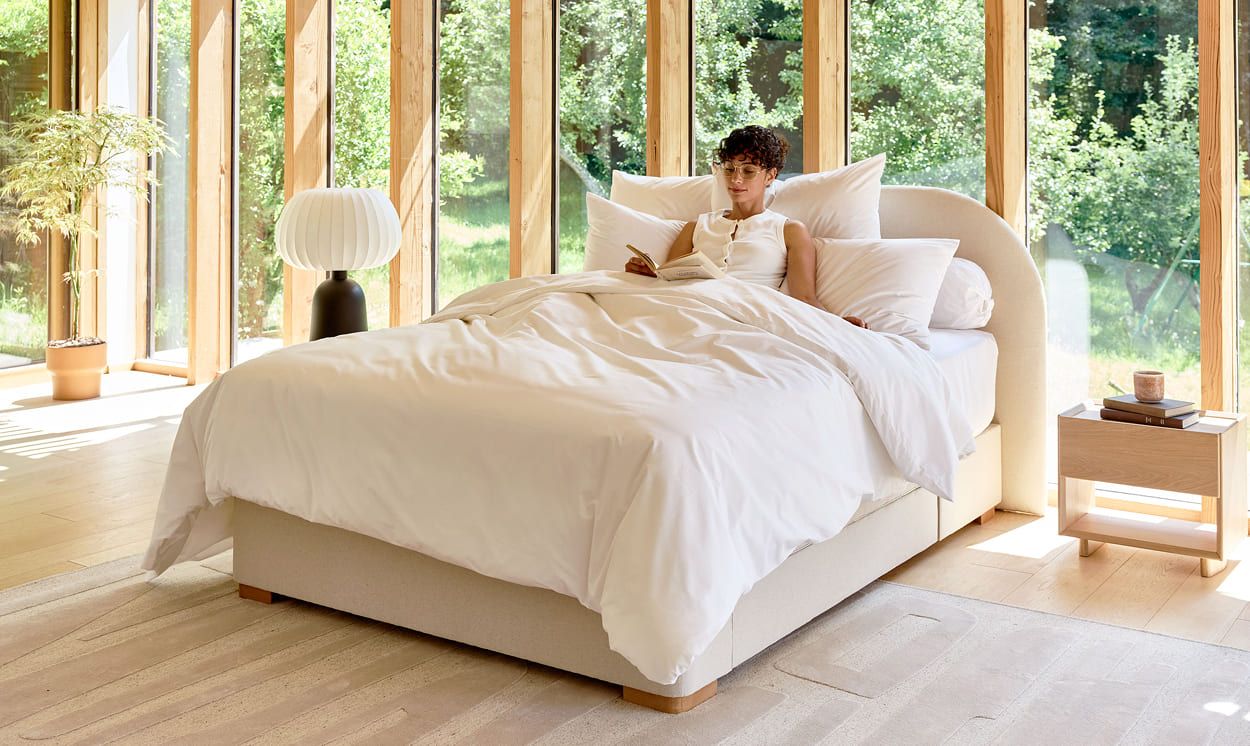 personne assise dans un lit, appuyée sur des oreillers, lisant dans une chambre lumineuse et calme, illustrant un rituel apaisant avant de dormir avec une hernie discale