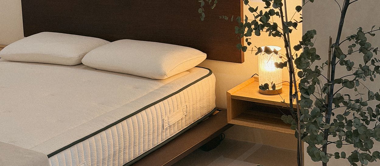 Chambre apaisée avec un lit, un matelas en latex naturel et une lampe diffusant une lumière chaude et tamisée, créant un environnement propice au sommeil.