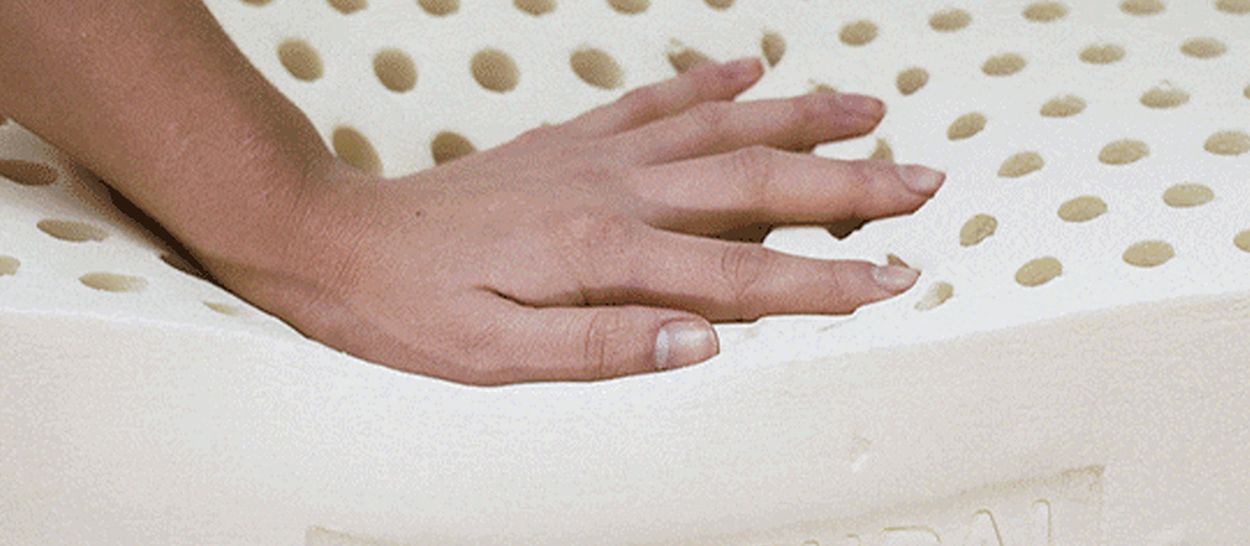 Main posée sur un matelas en latex naturel perforé, illustrant l’élasticité de la matière, la répartition des points de pression et la respirabilité.