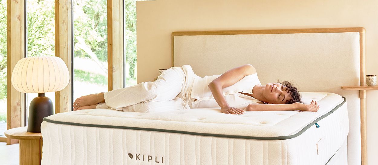 Femme allongée sur un matelas Kipli en latex naturel, dans une chambre apaisée, illustrant l’univers de la marque et l’origine du nom Kipli.