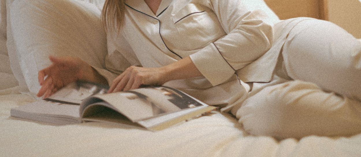 Personne allongée dans un lit lisant et écrivant dans un carnet avant de dormir, pour apaiser l’esprit et favoriser l’endormissement