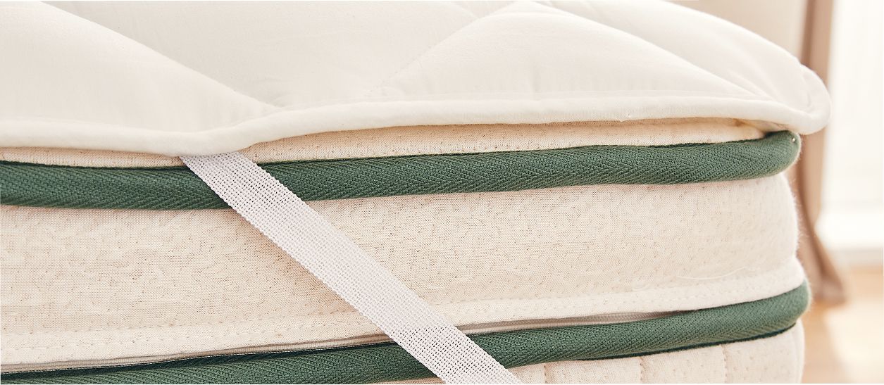 Gros plan sur l’épaisseur d’un surmatelas naturel fixé sur un matelas pour améliorer le confort et protéger la literie