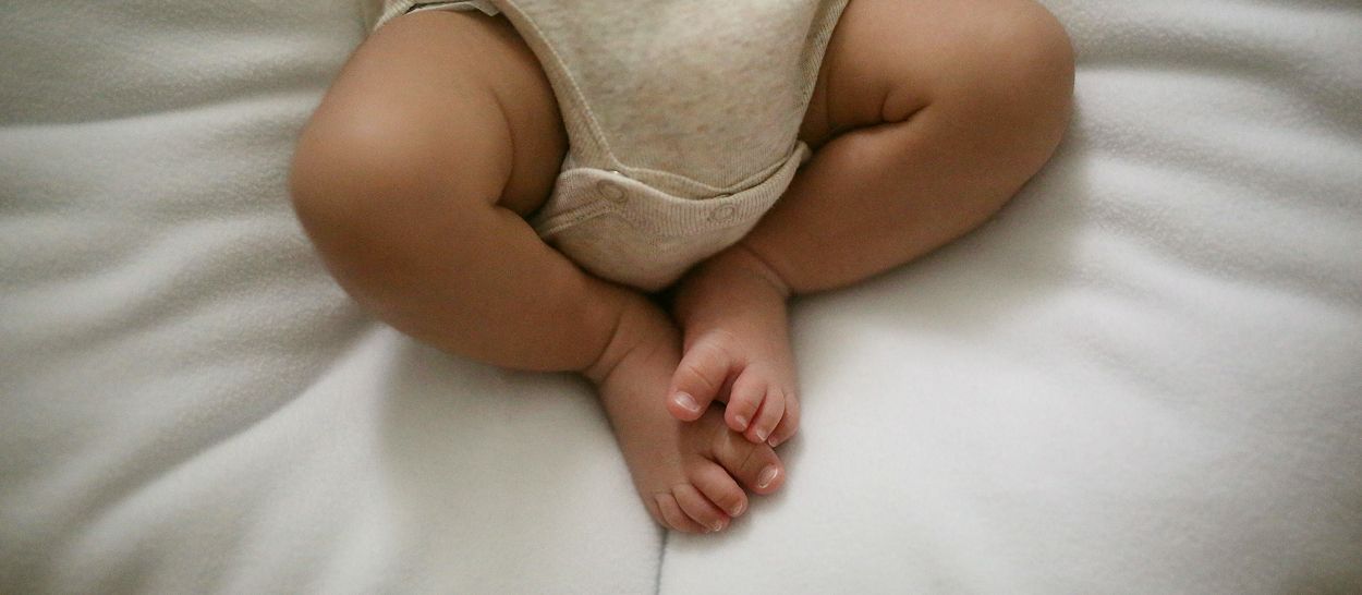 Jambes et pieds de nourrisson posés sur un textile blanc, body coton naturel
