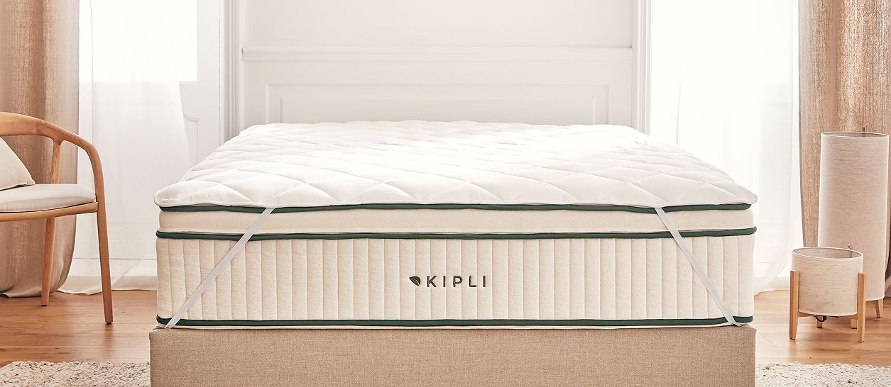 Surmatelas naturel installé sur un matelas Kipli dans une chambre lumineuse pour un confort de couchage durable