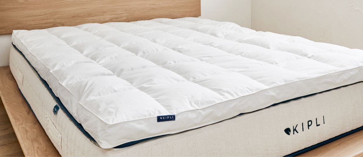 Surmatelas en plumes et duvet posé sur un matelas, offrant un accueil moelleux et enveloppant