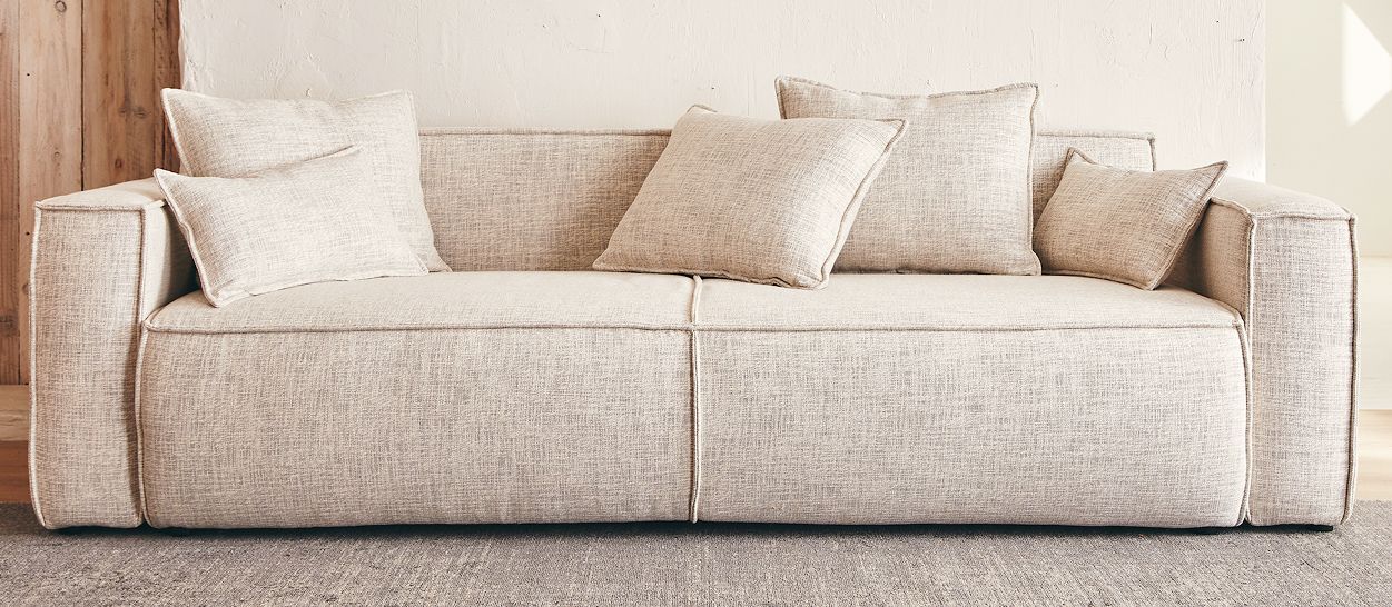 Canapé grand format en tissu beige texturé, assise profonde et large, coussins structurés