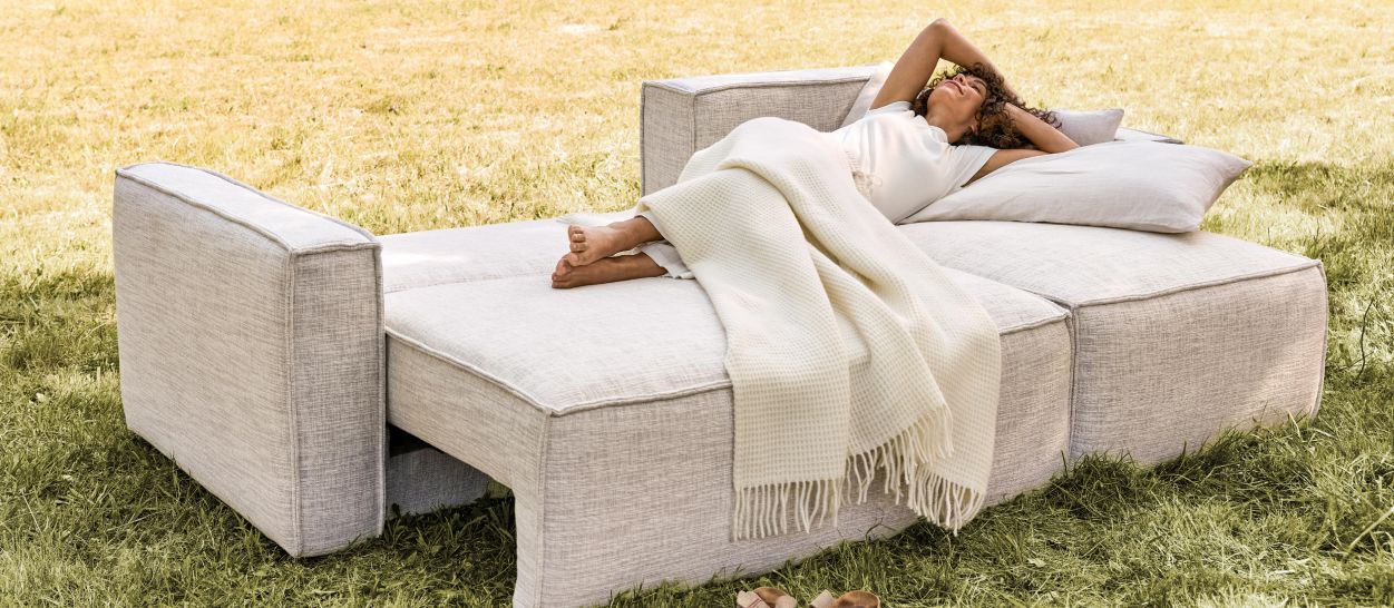 Femme allongée sur un canapé modulable en lin beige, plaid naturel, usage couchage en extérieur