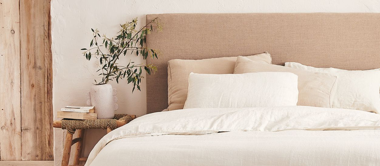 Tête de lit tapissée chanvre beige, linge lin blanc écru, tabouret bois brut, chambre apaisante