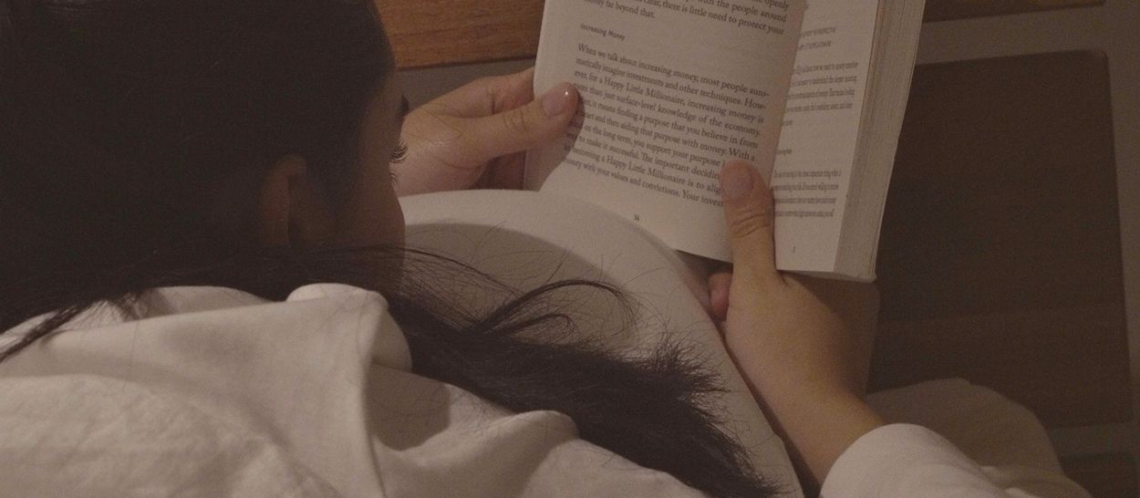 Personne allongée dans un lit lin blanc, lisant un livre, literie naturelle, moment de détente