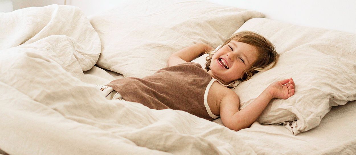 Enfant endormi paisiblement sur lit en lin blanc, sourire aux lèvres, literie naturelle douce