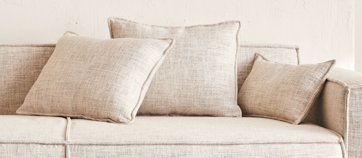 Trois coussins en tissu lin beige de formats différents sur un canapé, garnissage latex naturel