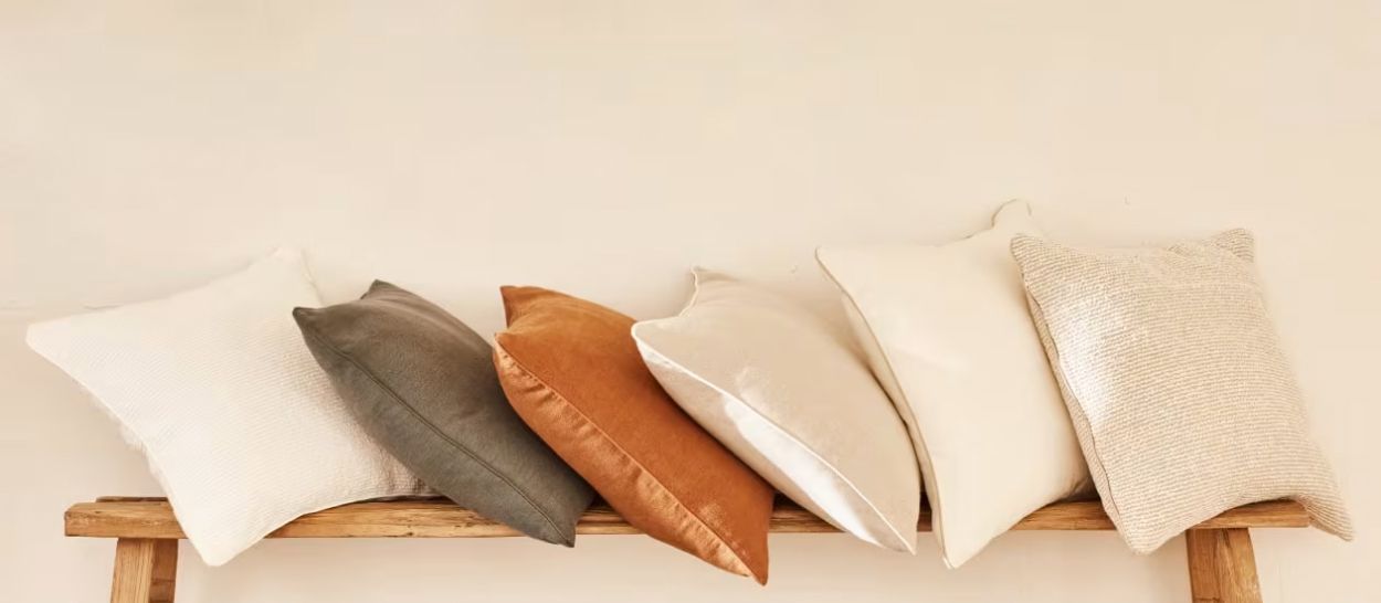 Six coussins en fibres naturelles variées alignés sur un banc bois, lin chanvre et coton Kipli