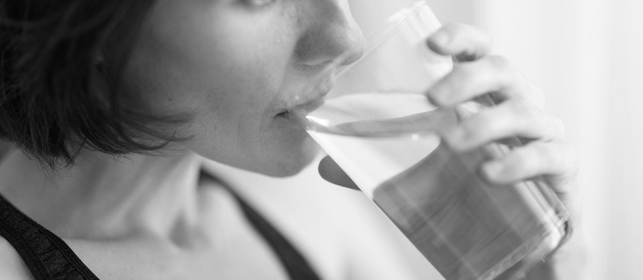 Femme buvant un verre d'eau, geste d'hydratation pour prévenir les crampes musculaires