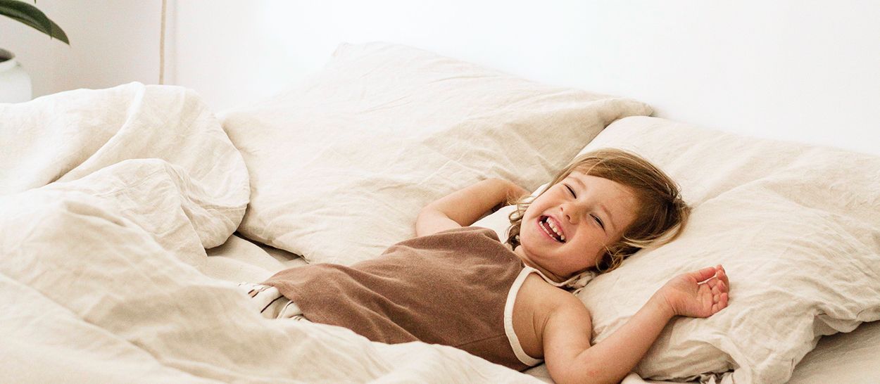 Enfant souriant allongé sur linge de lit blanc coton biologique frais, nuits fraîches et paisibles