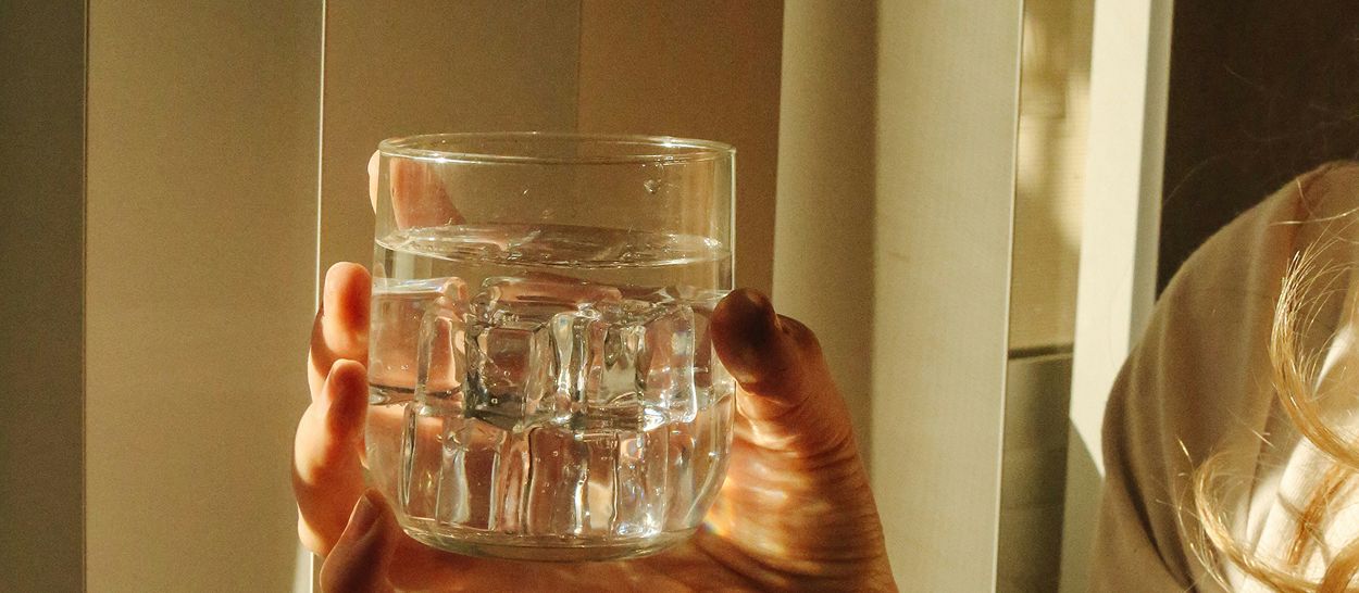 Main tenant un verre d'eau claire avec glaçons, hydratation et facteurs protecteurs du sommeil