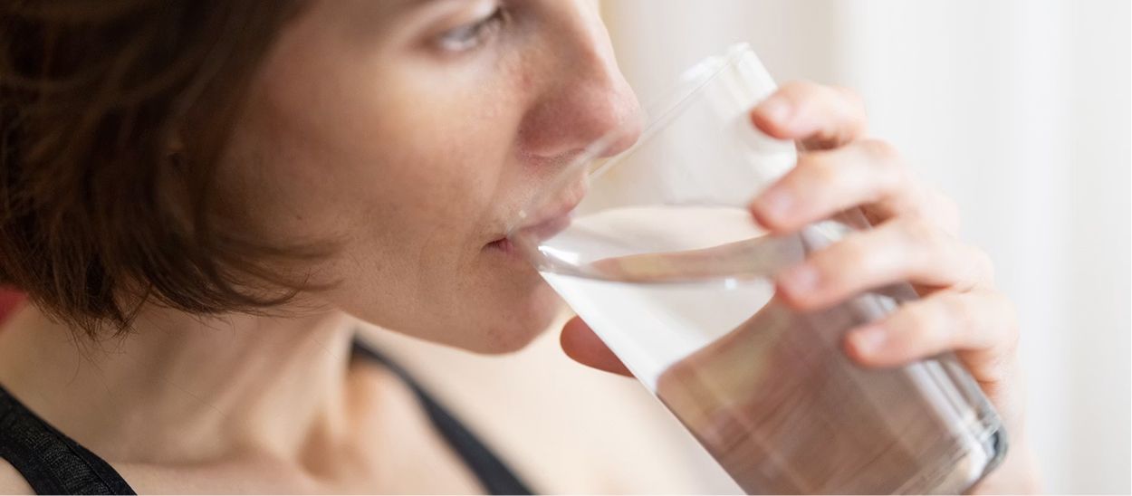 Personne buvant un verre d'eau fraîche avant de se coucher, illustrant l'importance des gorgées d'eau régulières en période chaude pour bien dormir