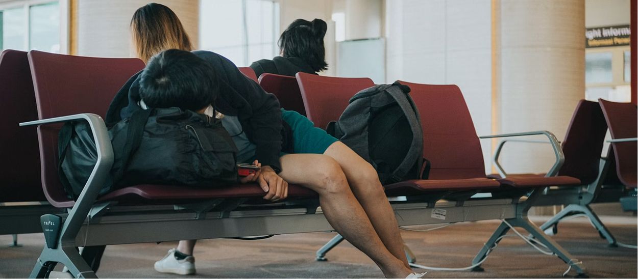 Voyageur fatigué endormi sur les chaises d'une salle d'attente d'aéroport avec bagages, illustrant l'épuisement et l'importance de bien gérer la récupération après un long vol avec décalage horaire