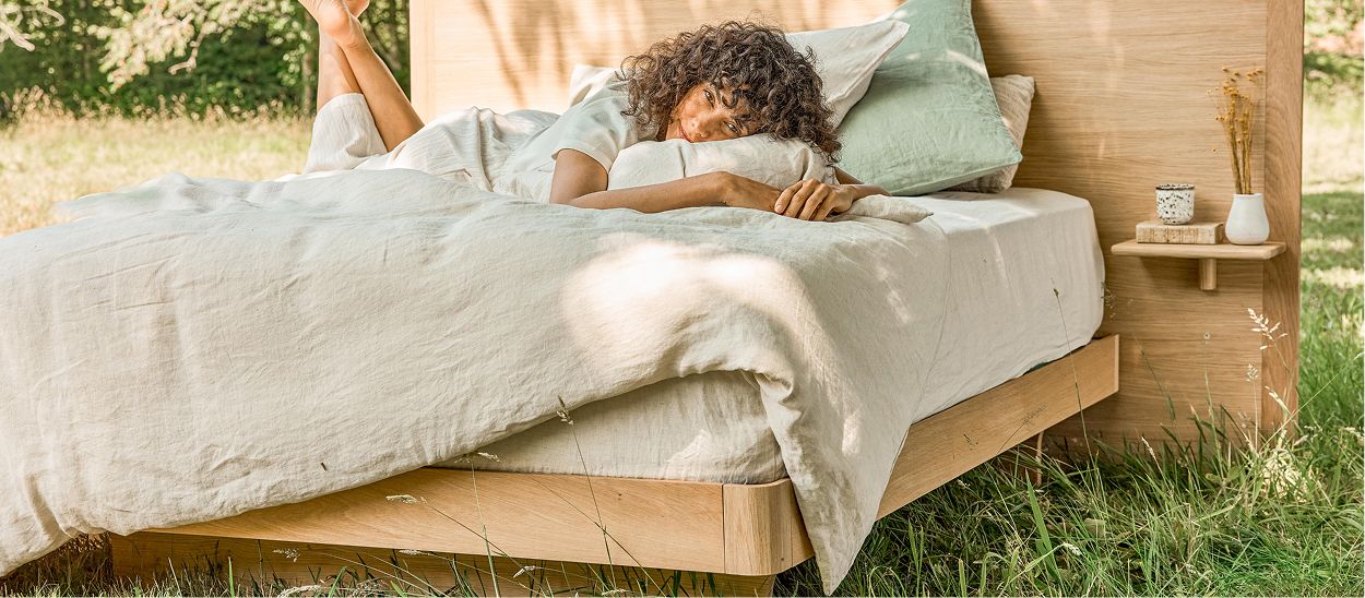Femme allongée sur un lit en bois massif Kipli équipé d'un matelas naturel en extérieur.