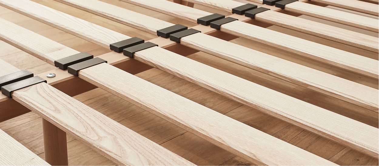 Vue rapprochée des lattes en bois flexibles d'un sommier, illustrant leur rôle dans le soutien du matelas.
