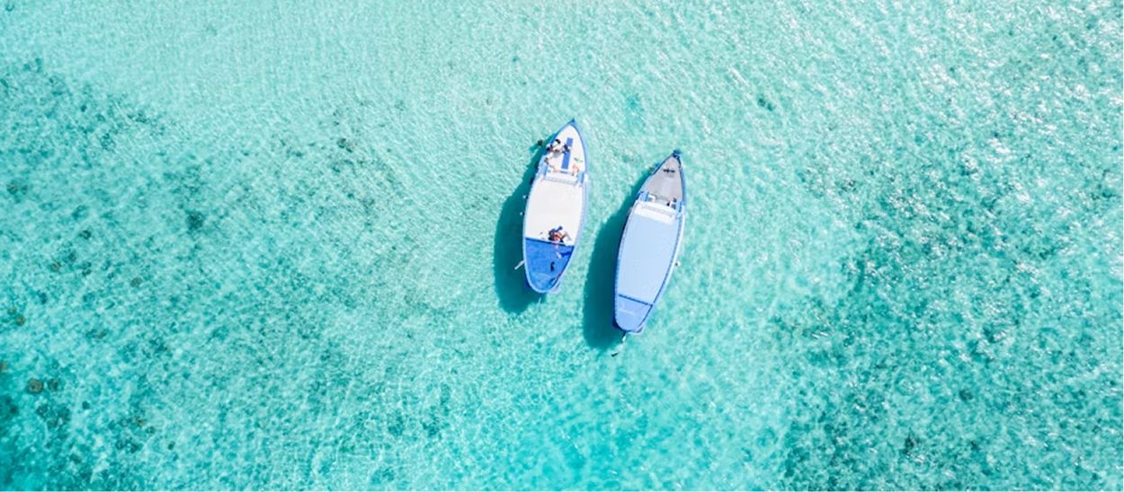 Vue aérienne de deux bateaux blancs sur eau turquoise et cristalline en destination tropicale, illustrant les magnifiques destinations lointaines accessible par long-courrier malgré le décalage horaire