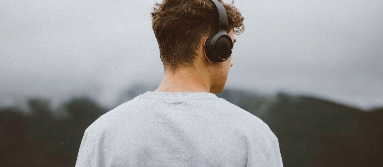 Homme de dos portant un casque audio en extérieur face à un paysage brumeux, illustrant le masquage sonore par le bruit blanc qui couvre les bruits environnants pour favoriser l'endormissement
