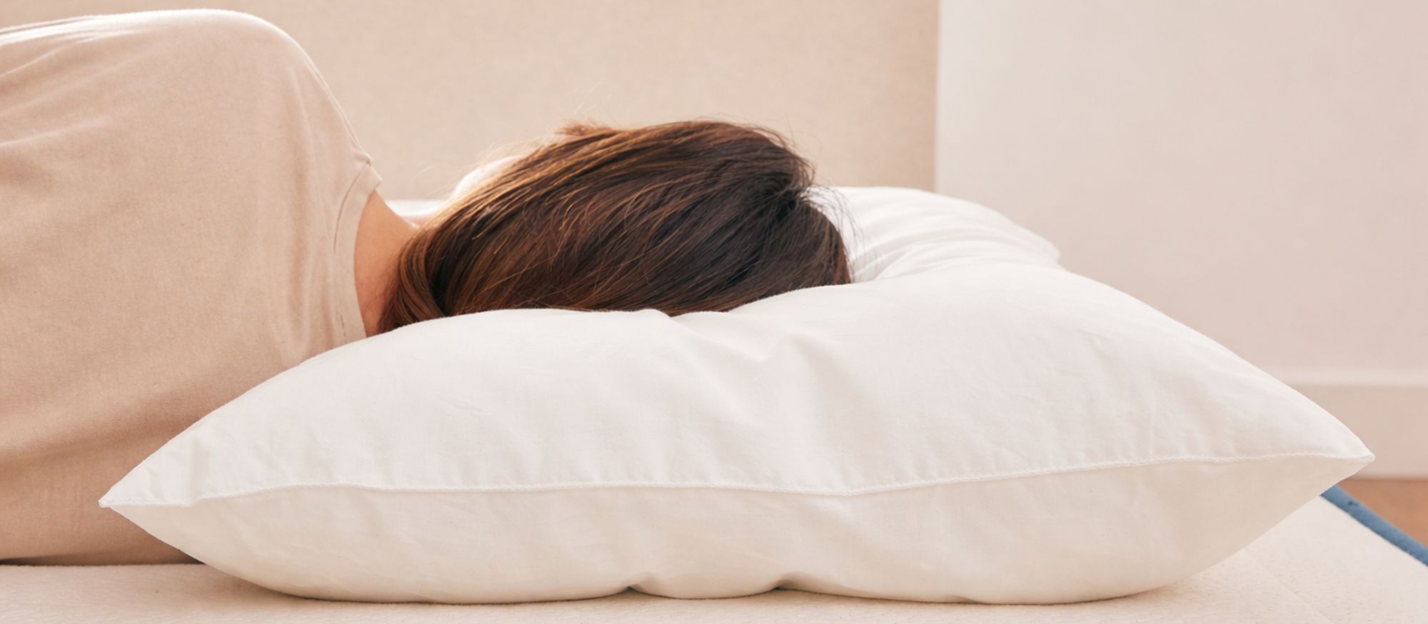 Femme dormant sur le côté, la tête enfoncée dans un oreiller moelleux qui s'écrase sous son poids, illustrant l'impact de la fermeté d'un oreiller sur le maintien de la tête et l'importance d'une matière qui garde sa hauteur comme le latex naturel
