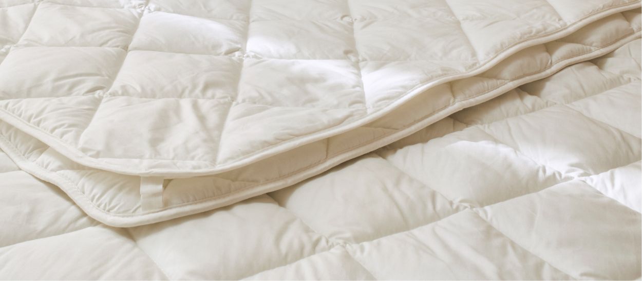 Gros plan sur une couette 4 saisons Kipli laissant voir ses deux couettes matelassées superposées et le système de ficelles cousu qui les relie, illustrant l'assemblage modulable pour adapter la chaleur à chaque saison