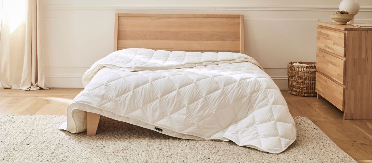 Couette 4 saisons blanche déployée sur un lit en bois massif dans une chambre épurée aux tons naturels, illustrant une couette naturelle en Tencel et coton biologique, durable et facile à entretenir