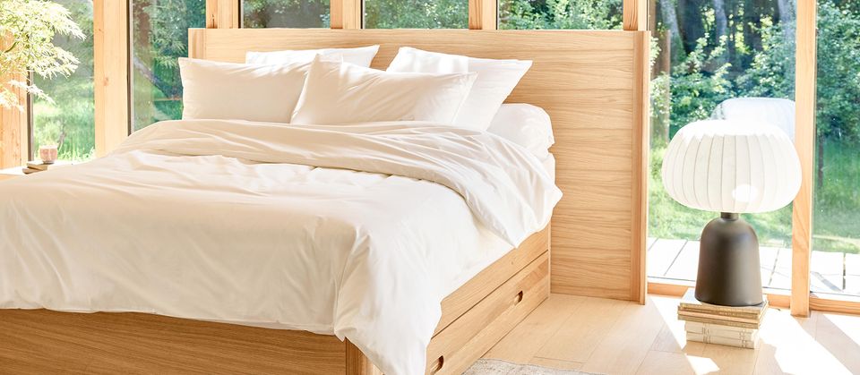 Chambre lumineuse avec lit en bois massif clair, linge blanc, baies vitrées, environnement sain
